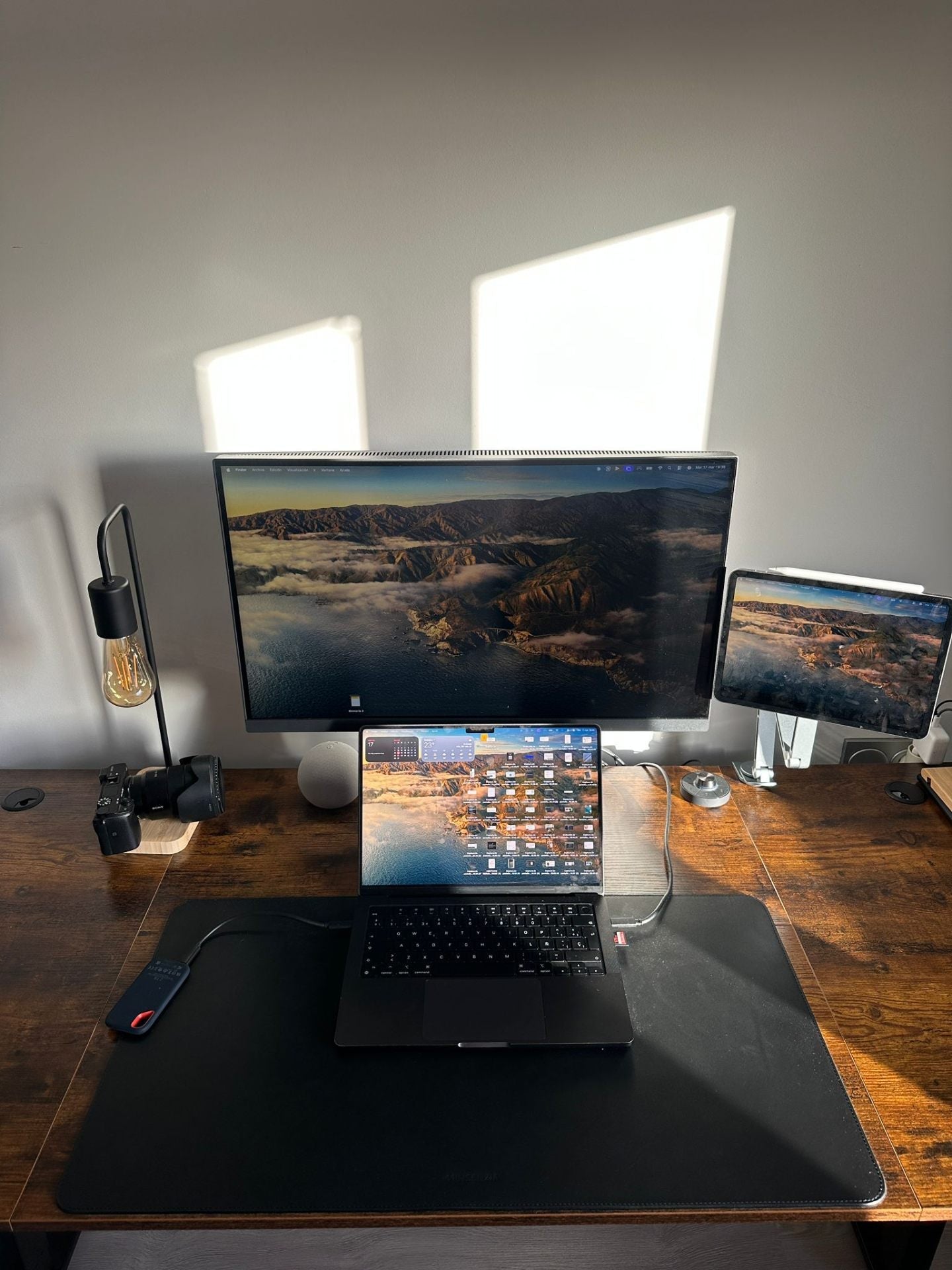Escritorio de madera con un MacBook sobre una alfombrilla de piel Minsenzia, a la luz natural, sin móvil a la vista.